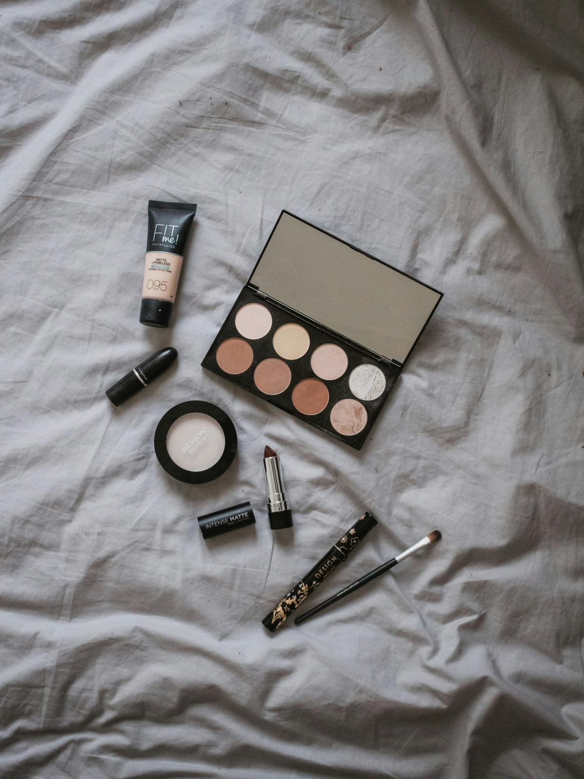 A flat lay of foundation, an eyeshadow palette and makeup brushes